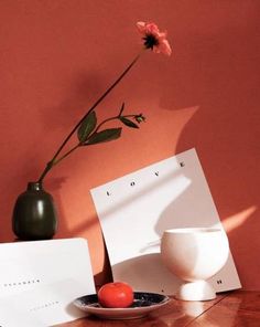 a vase with a flower and two cards on a table next to a bowl full of tomatoes