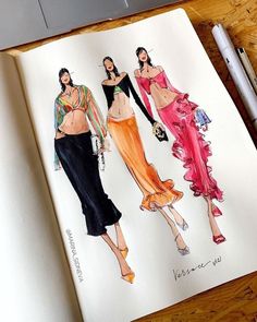 an open notebook with drawings of women in different outfits on it, along with a pen and marker