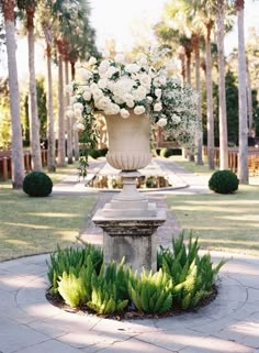 a large vase with white flowers is in the middle of a walkway surrounded by palm trees