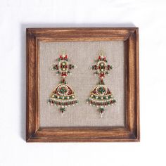 a pair of earrings is displayed in a wooden frame on a white wall behind it