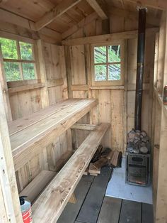 the inside of a small wooden cabin with wood stacked on the floor and shelves next to it