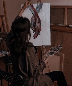 a woman is painting on an easel with her hands in front of the easel