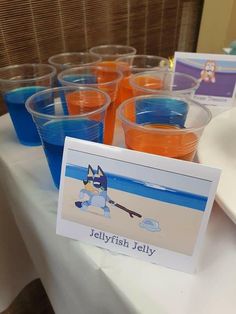 plastic cups filled with orange and blue liquid sitting on top of a white tablecloth