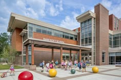 many people are walking in front of a school with large balls on the ground outside