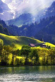 the mountains are covered in green grass and trees, with a small house on the other side