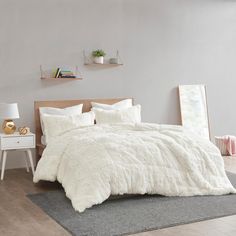 a bed with white comforter and pillows in a room next to a table on the floor