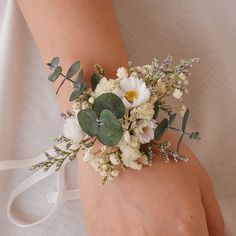 a woman's hand holding a bouquet of flowers and greenery on her wrist