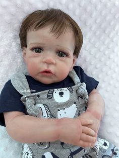 a baby doll that is laying down on a white blanket and looking at the camera