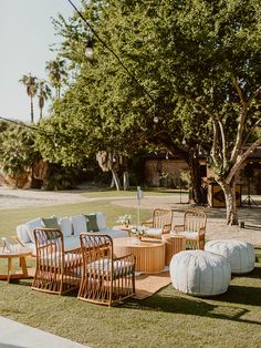 an outdoor seating area with chairs, tables and round ottomans on the grass in front of a tree