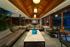 a living room filled with lots of furniture next to a large glass window covered wall