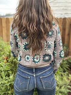 a woman with long hair standing in front of a fence wearing jeans and a sweater