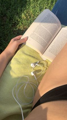 a woman laying on the grass reading a book with headphones attached to her leg