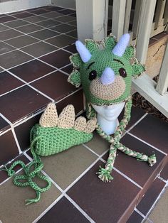 a crocheted green dragon stuffed animal sitting on the ground next to a door