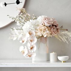 a vase filled with flowers sitting on top of a white shelf next to a clock