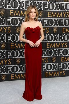 a woman in a long red dress standing on a gray carpet with an embellished wall behind her