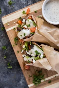 some food is sitting on a cutting board next to a bowl of ranch dressing and sauce