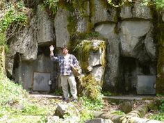 a man standing in front of a rock formation with moss growing on it's sides