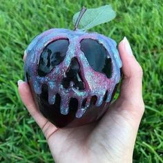 a hand holding an apple shaped like a skull on top of green grass with blue and pink glaze