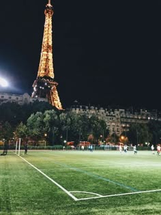 people playing soccer in front of the eiffel tower at night with lights on