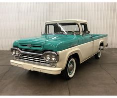 an old green and white pickup truck parked in a garage next to a metal wall