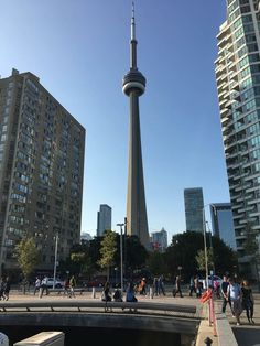 people are walking on the sidewalk in front of tall buildings and a bridge with a spire