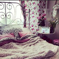 a bed with pink and white comforter next to a laptop computer on a table