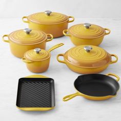 yellow cast iron pots and pans on a white countertop with black skillets