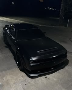 a black car parked in the middle of a parking lot at night with lights on