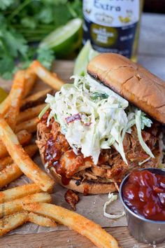 a pulled pork sandwich with coleslaw and ketchup next to french fries