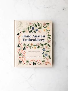 the book jane austen embroidery is sitting on a marble surface with flowers and leaves