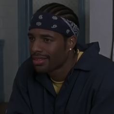 a man with a bandana on his head sitting in front of a wall and looking at the camera