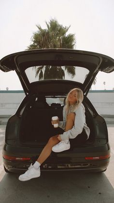 a woman sitting in the back of a car holding a coffee cup and looking into the trunk