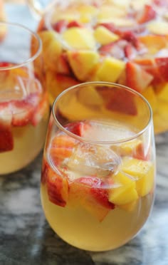 two glasses filled with fruit sitting on top of a marble counter next to each other