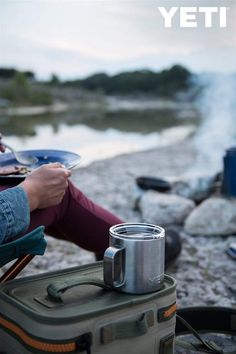 a person sitting in a chair next to a campfire with a cup on it