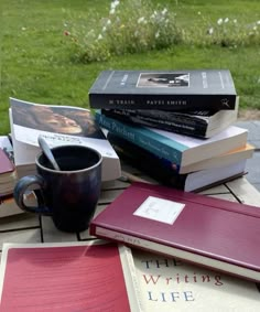 a table with books and a coffee cup on top of it in front of a grassy area