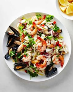 a white plate topped with shrimp and clams next to lemon wedges on a table