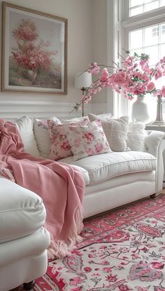 a living room filled with white furniture and pink flowers on the window sills