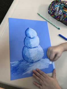 someone is drawing a snowman with colored pencils on a piece of blue paper