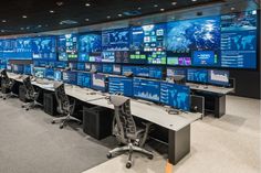 rows of computer monitors in an office with chairs and screens on the wall behind them