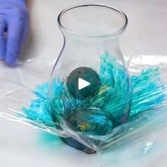 a glass vase filled with blue and green feathers on top of a white tablecloth