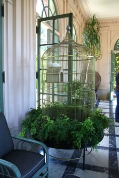 a bird cage sitting on top of a table next to a chair and potted plant