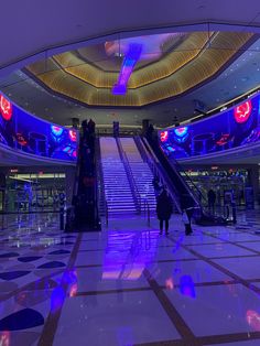 an escalator in the middle of a building with blue lights and people walking up it