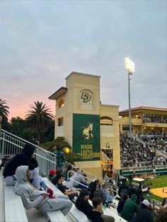 people are sitting on bleachers at a baseball game as the sun goes down