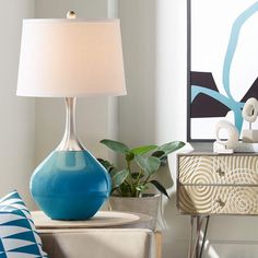 a blue lamp sitting on top of a table next to a white vase with a plant in it