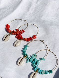 three pairs of hoop earrings with shells and coral beads on white fabric background, closeup