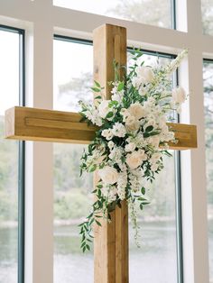 a cross decorated with white flowers and greenery in front of large windows overlooking water