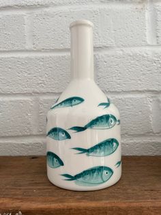 a vase with fish painted on it sitting on a wooden table next to a brick wall