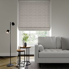 a white couch sitting next to a window in a living room under a roman blind