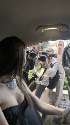 a woman sitting in the back seat of a car with cameras around her and people taking pictures