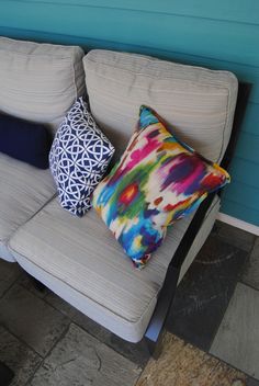 three colorful pillows sitting on top of a gray couch next to a blue and white wall